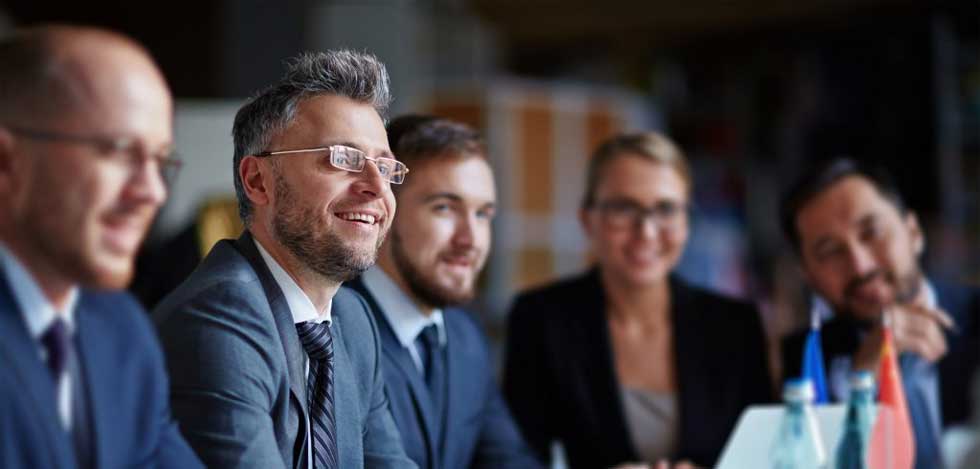 Photo of five business people wearing suits, smiling and gathered together as a team